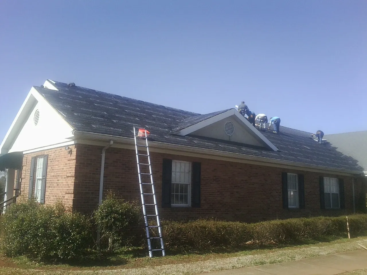 Crew tearing shingles off a brick ranch roof with a ladder set — Emergency Roof Repair work by our crew in Harris